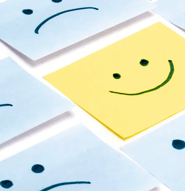 Pozytywne myślenie i optymizm symbolizowane uśmiechniętą karteczką wśród smutnych emocji